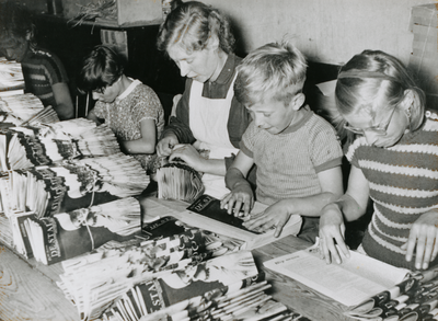 876620 Portret van een zelatrice die met enkele kinderen tijdschriften 'De Stad Gods' aan het vouwen is voor verdere ...